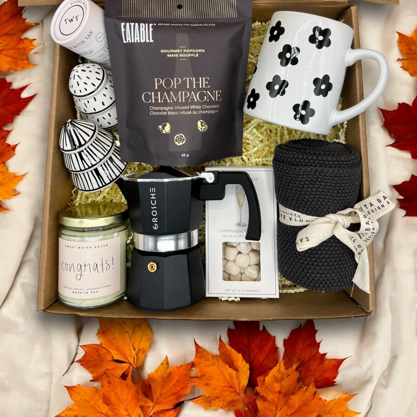 Congrats basket filled with Congrats candle, espresso machine, salt & pepper shakers, champagne popcorn, mug, dish towel, champagne candies and tea.