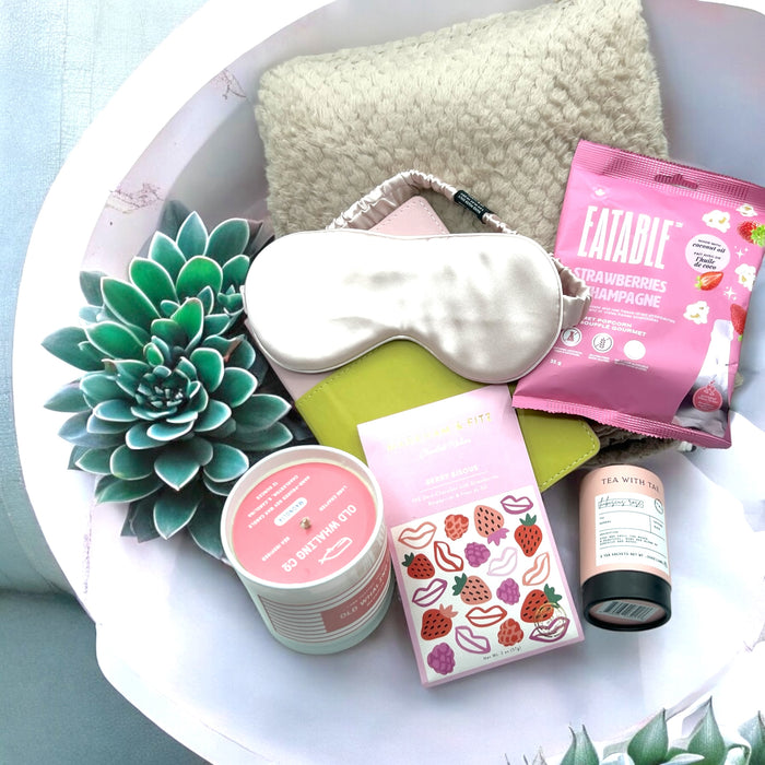 Gift basket with popcorn, tea, artisan chocolates, a magnolia candle, face mask, cozy blanket, and vegan journal; ships nationwide from NYC.
