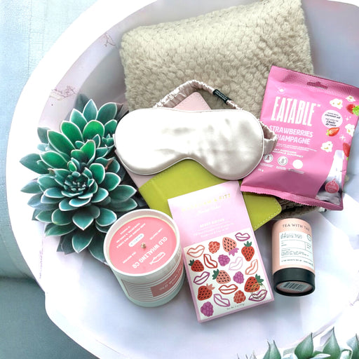 Gift basket with popcorn, tea, artisan chocolates, a magnolia candle, face mask, cozy blanket, and vegan journal; ships nationwide from NYC.
