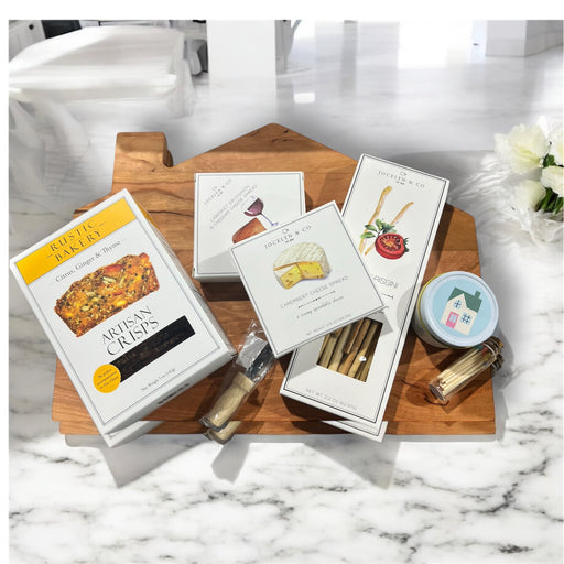 Cozy cabin cutting board with assorted crackers and cheeses, house candle and cutting knife. Makes a great housewarming gift.