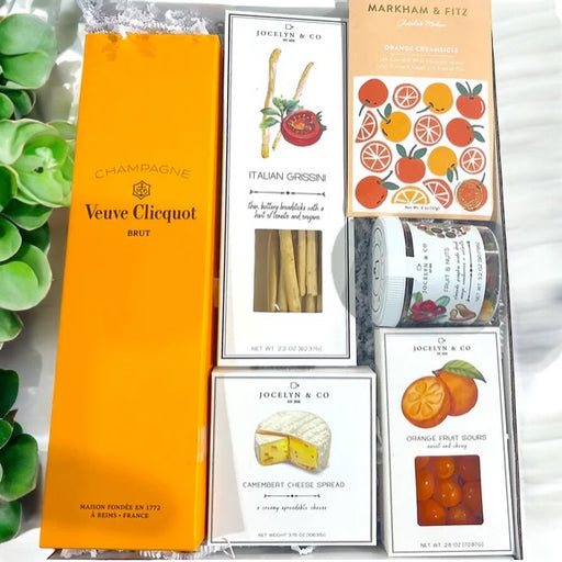 Gift box contains Veuve Clicquot Champagne, breadsticks, cheese, orange candies, mixed nuts and artisan white chocolate bar.